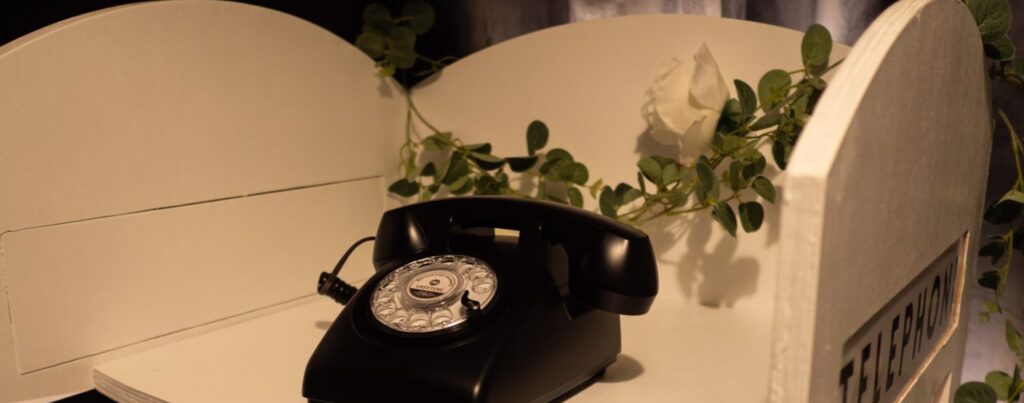 a white phone box stand with a black dial phone set up for audio guest book at a wedding