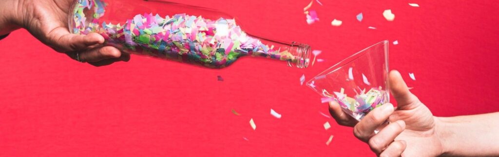 two people celebrating with confetti in a wine bottle