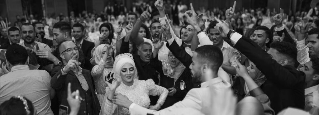 greyscale image of large group of guests at an arabic wedding, wedding party central having a wedding dance off