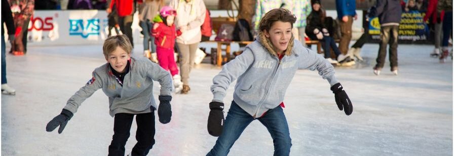2 children ice skating on an ice rink with other people skating in the background