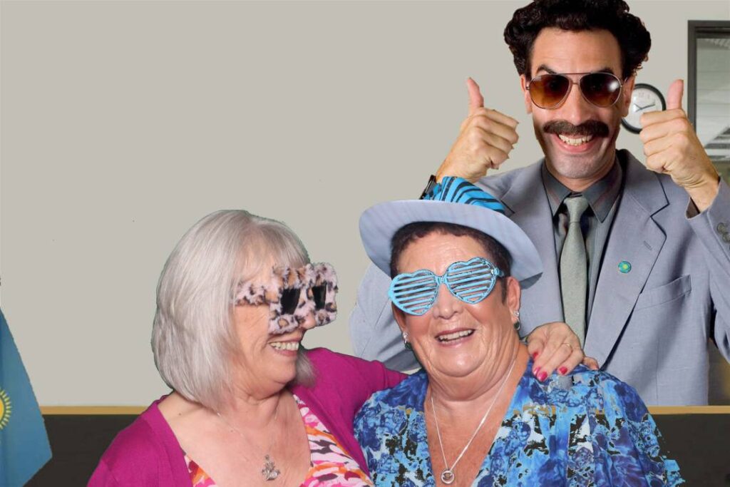 2 woman with props taking a picture on a green screen booth with borat theme