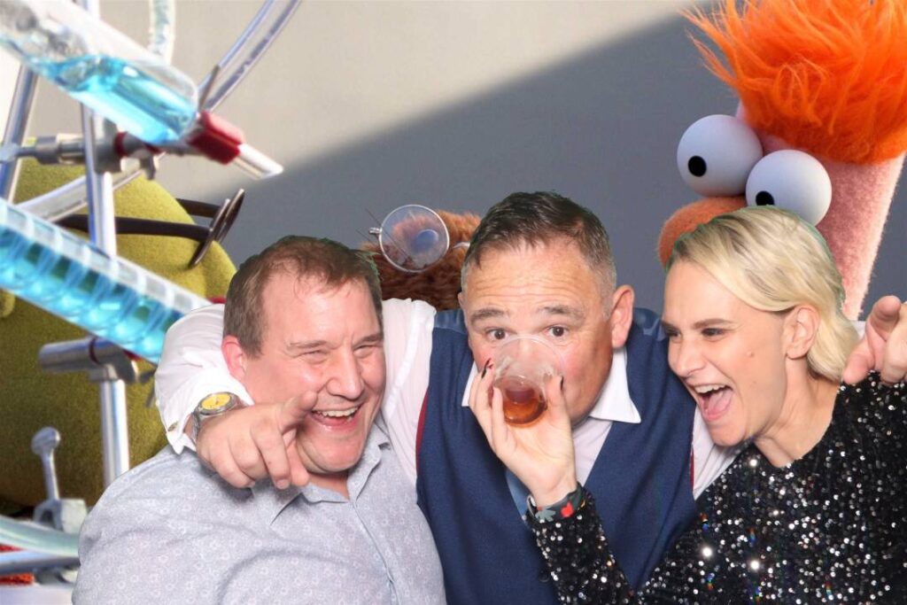 group of people laughing and drinking in front of a green screen photo booth with elmo theme