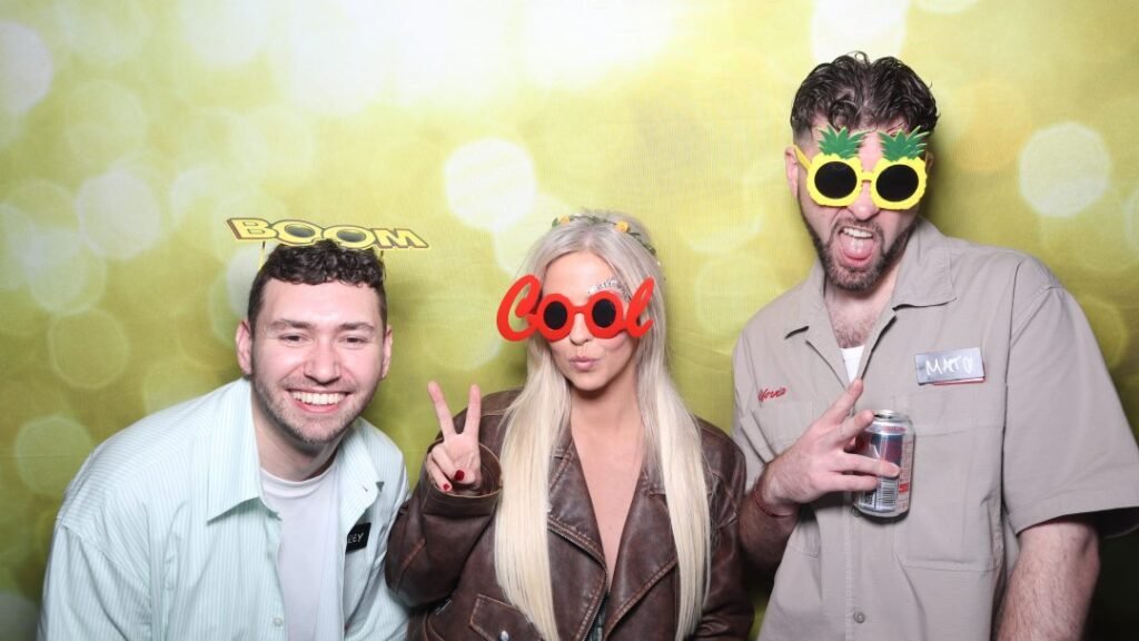 two men and a woman in front of a photo booth with props